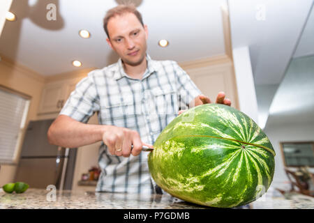 Gros plan du jeune homme tenant, la réduction de moitié, les moitiés avec grand couteau, big, ripe melon à la maison, maison, appartement sur les comptoirs de cuisine Banque D'Images