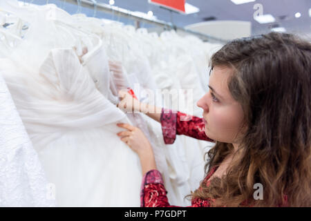 Jeune femme recherche, essayant sur, le choix, le toucher des robes en boutique discount magasin de vêtements blancs pendaison de crémaillère sur ligne cintres Banque D'Images