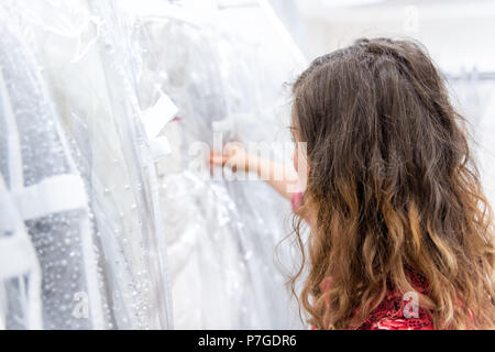 La recherche d'une femme, en essayant sur, le choix, le toucher des robes en boutique discount magasin de vêtements blancs pendaison de crémaillère sur cintres dans rangée Banque D'Images