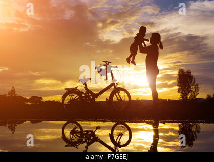 Reflet Silhouette de mère avec son enfant contre le coucher du soleil et vélo. L'activité de la famille asiatique de vie. Banque D'Images