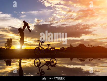 Reflet Silhouette de mère avec son enfant contre le coucher du soleil et vélo. L'activité de la famille asiatique de vie. Banque D'Images