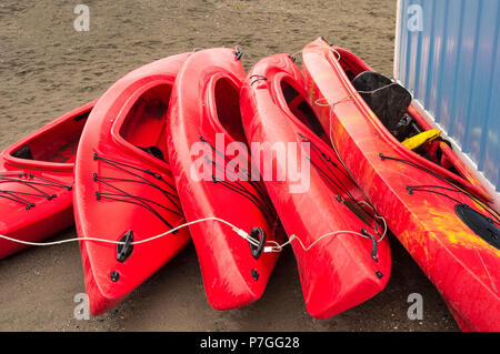 Plastique rouge vide à louer des kayaks récréatifs ou de voitures, stockés sur une plage de sable un jour de pluie. La plage Crescent, Surrey, Colombie-Britannique, Canada. Banque D'Images