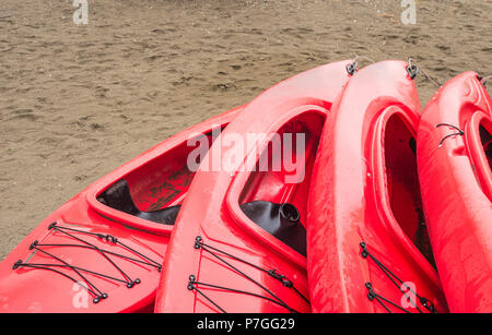 Plastique rouge vide à louer des kayaks récréatifs ou de voitures, stockés sur une plage de sable un jour de pluie. La plage Crescent, Surrey, Colombie-Britannique, Canada. Banque D'Images