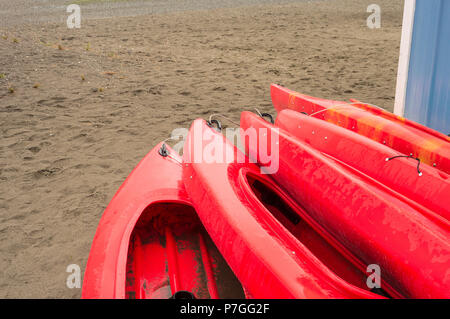 Plastique rouge vide à louer des kayaks récréatifs ou de voitures, stockés sur une plage de sable un jour de pluie. La plage Crescent, Surrey, Colombie-Britannique, Canada. Banque D'Images