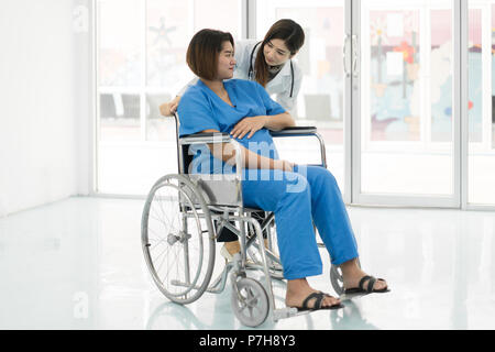 Asian Woman Doctor talking to young pregnant woman en fauteuil roulant à l'hôpital. Belle asiatique médecin prendre soin des patients en fauteuil roulant. Banque D'Images