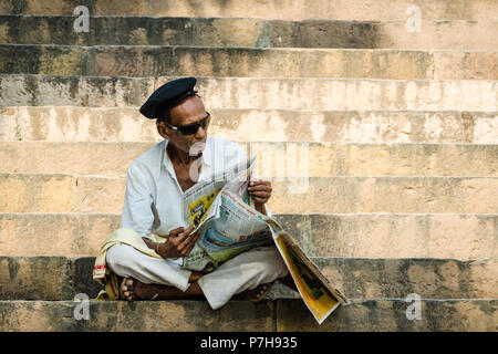 L'homme indien lire un journal sur les marches des Ghats de Varanasi, Inde Banque D'Images