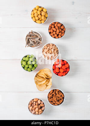 Les collations salées. Assortiment de différents snack pour la bière, le vin. Vitrage arachides, pistaches, chips, crackers, le poisson dans un petit bol sur la table en bois blanc. V Banque D'Images