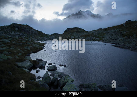 Lac de montagne le matin à l'Pfitscherjoch (col) dans le Tyrol du sud avec vue sur les sommets Rotbachlspitze (crête), les nuages, l'obscurité, le froid Banque D'Images