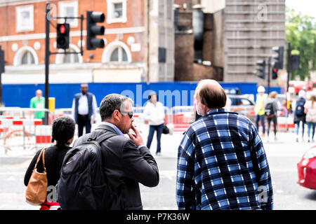 Londres, Royaume-Uni - 21 juin 2018 : retour de deux hommes, le tabagisme les piétons attendent le feu rouge par la construction sur street road à trajet du matin dans ce Banque D'Images