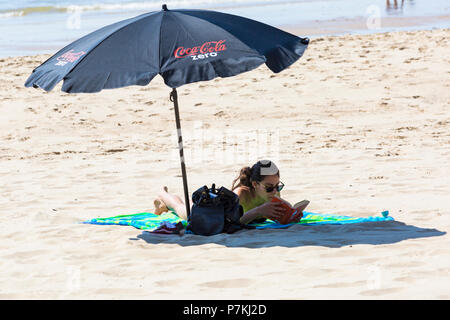 Bournemouth, Dorset, UK. 7 juillet 2018. Météo France : un autre jour ensoleillé chaud comme la canicule continue et des milliers de tête sunseekers au bord de la mer pour profiter de la plages de sable de Bournemouth. Jeune femme lisant un livre à l'ombre d'un parasol parasol. Credit : Carolyn Jenkins/Alamy Live News Banque D'Images