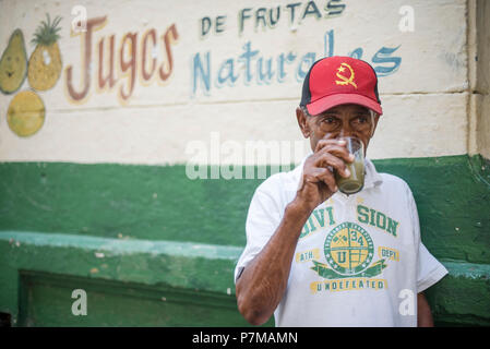 Un homme boit guarapo, une boisson sucrée faite de la canne à sucre pressée, en dehors d'un stand de fruits à La Havane. Banque D'Images