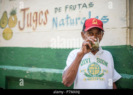 Un homme boit guarapo, une boisson sucrée faite de la canne à sucre pressée, en dehors d'un stand de fruits à La Havane. Banque D'Images