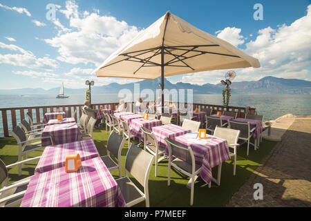 Les tables d'un petit restaurant au bord du lac de Torri del Benaco sur la rive orientale du lac de Garde, Vérone, Vénétie, Italie province, Banque D'Images