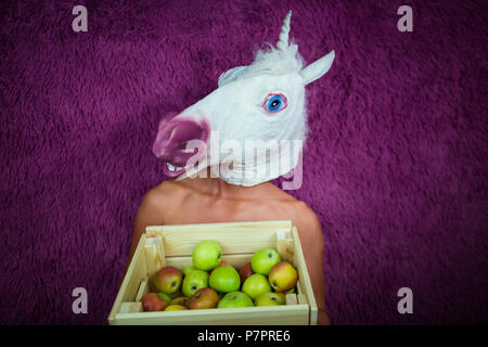 Freaky jeune femme se tient sur le fond violet avec caisse de pommes. Funny Girl est titulaire d'Unicorn de fruits dans les mains. Portrait de Dame inhabituelle. Banque D'Images