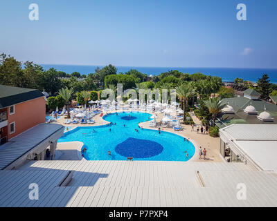 Vue aérienne de la Méditerranée et de la ligne d'horizon et grande piscine ronde avec des palmiers, des chaises longues et un restaurant Banque D'Images
