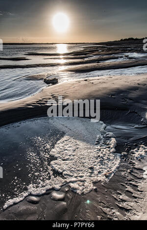 Le lever du soleil sur la boue et la mousse qui s'est formée sur une flaque d'eau à marée basse dans la baie de Somme Banque D'Images