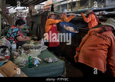 La collecte des déchets avec femme continue à préparer la nourriture malgré la présence de l'éboueurs vidange d'un skip to chargé avec des ordures. Thaïlande Banque D'Images