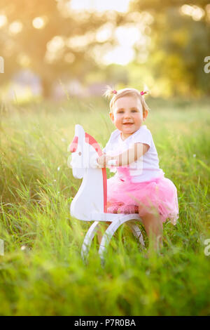 Belle petite fille en robe rose équitation sur cheval jouet en bois à l'extérieur Banque D'Images