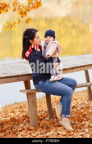 Jeune mère avec ma petite fille à l'automne forêt près de la rivière. Maman holding baby girl in hands Banque D'Images