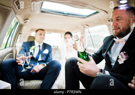 Groomsman ouverture du flacon et verser dans des verres champagni dans la voiture. Banque D'Images