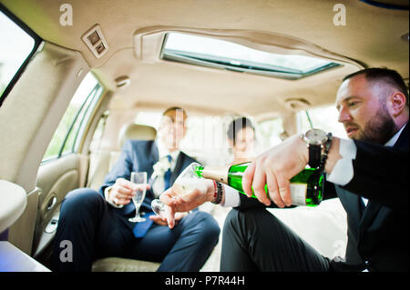 Groomsman ouverture du flacon et verser dans des verres champagni dans la voiture. Banque D'Images