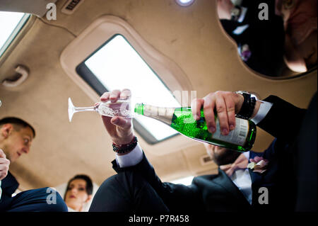 Groomsman ouverture du flacon et verser dans des verres champagni dans la voiture. Banque D'Images