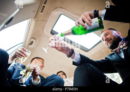 Groomsman ouverture du flacon et verser dans des verres champagni dans la voiture. Banque D'Images