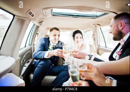 Garçons et filles avec wedding couple drinking champagne dans la voiture. Banque D'Images