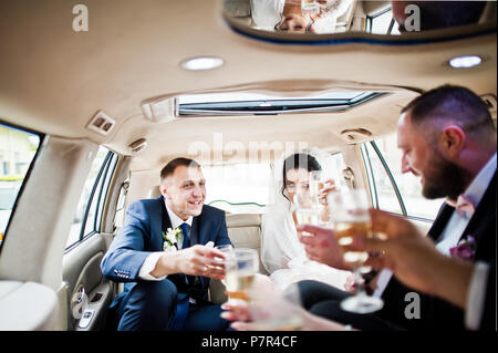 Garçons et filles avec wedding couple drinking champagne dans la voiture. Banque D'Images