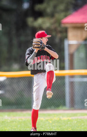 La prestation de Pitcher la hauteur, en pleine course, les garçons d'après-midi d'un match de baseball junior. Cranbrook, BC. Banque D'Images