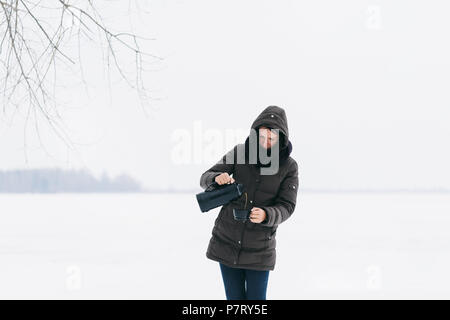 Femme en vêtements d'hiver sur paysage enneigé verse de café thermos Banque D'Images