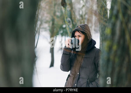 Femme en vêtements d'hiver de boire du café dans la forêt enneigée Banque D'Images