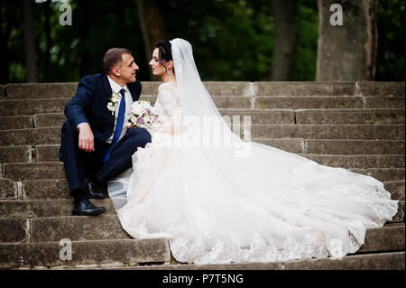 Couple nouvellement marié assis dans le parc sur le versant ensoleillé de l'été jour de mariage. Banque D'Images