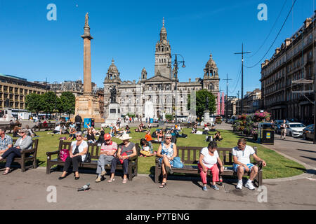 Personnes bénéficiant d'une agréable soirée ensoleillée à George Square, Glasgow central, avec la Ville des chambres dans l'arrière-plan, le cénotaphe, et des statues, Banque D'Images