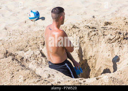 Bournemouth, Dorset, Royaume-Uni. 8 juillet 2018. Météo au Royaume-Uni : un autre jour chaud ensoleillé alors que la vague de chaleur se poursuit et des milliers de demandeurs de soleil se rendre au bord de la mer pour profiter des plages de sable de Bournemouth sur la côte sud. Jeune homme creusant un trou profond dans le sable. Crédit: Carolyn Jenkins/Alay Live News Banque D'Images