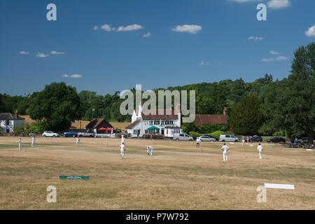 Tilford, Surrey, Royaume-Uni. 8 juillet 2018. Comme la vague de chaleur continue, les gens s'amusaient au soleil un beau dimanche après-midi dans le joli village de Tilford. Beaucoup étaient en train de se rafraîchir dans la rivière ou de bronzer, tandis qu'un match de cricket était joué sur le vert du village. Banque D'Images