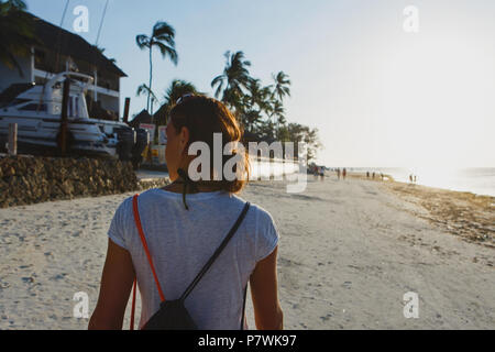 Vue de l'arrière jeune femme avec sac à dos, marcher le long du rivage de l'océan au coucher du soleil Banque D'Images