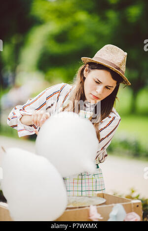 Thème photo sucreries de petite entreprise. Une jeune femme de race blanche avec un tablier en négociant la hat le propriétaire de la sortie fait une barbe à papa, un procès équitable Banque D'Images