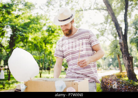 Thème photo sucreries de petite entreprise. Un jeune homme avec une barbe d'un négociant de race blanche dans le chapeau le propriétaire de la sortie fait la barbe à papa, fairy Banque D'Images