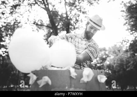 Thème photo sucreries de petite entreprise. Un jeune homme avec une barbe d'un négociant de race blanche dans le chapeau le propriétaire de la sortie fait la barbe à papa, fairy Banque D'Images