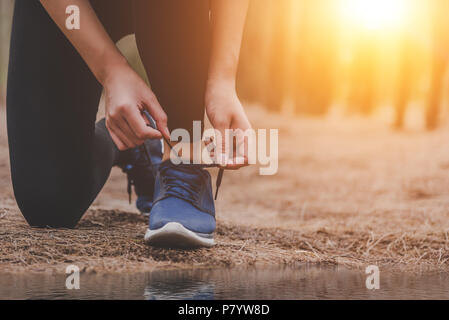 Jeune femme en cours de remise en forme à l'extérieur dans les lacets de liage arrière-plan de la forêt. Sport et Nature concept. Campagne de l'exercice et l'activité et de l'athlète Banque D'Images