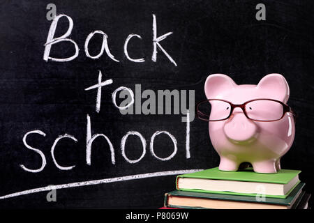 Pink piggy bank with glasses debout sur des manuels scolaires en face d'un tableau noir avec message retour à l'école. Banque D'Images