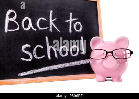Pink piggy bank avec des lunettes, debout devant un petit tableau noir avec message retour à l'école. Banque D'Images