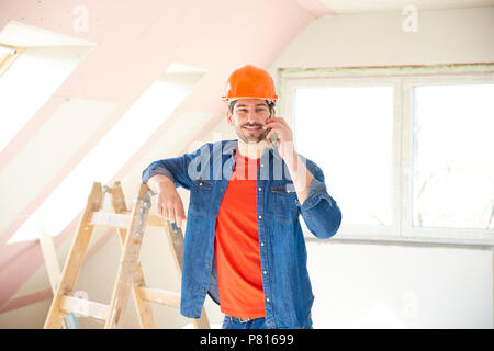 Beau jeune réparateur en utilisant son téléphone portable tout en se tenant dans la chambre et de travailler sur les réparations de l'intérieur. Banque D'Images