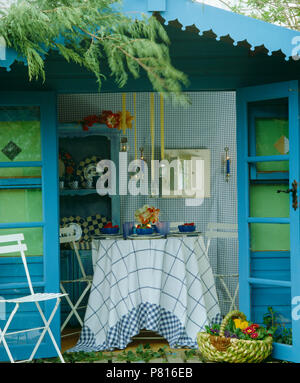 Abri de jardin bleu avec des portes ouvertes et de lanternes à bougie au-dessus de table de salle à manger avec un chiffon à carreaux blancs et bleus Banque D'Images