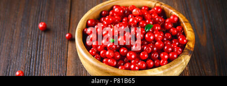 Airelle rouge, foxberry, canneberge, airelle rouge dans un bol en bois sur une table en bois brun. Banque D'Images