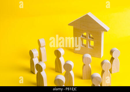 Un groupe de figures en bois de personnes entourent et regarder la maison en bois. Les jeunes à la recherche de logements abordables. Prêts et prêts pour le bon de com. Banque D'Images