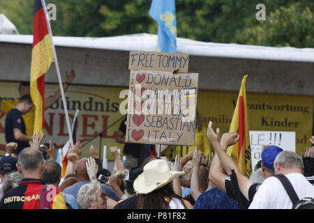 Kandel, Allemagne. 07Th Juillet, 2018. Les manifestants de droite écouter un discours au rassemblement, holding drapeaux allemands et un signe qui appelle à une libération de la militante d'extrême droite, Tommy Robinson et montre leur soutien à Donald Trump, Vladimir Poutine, Viktor Orban, Sebastian Kurz (Chancelier autrichien) et l'Italie. Autour de 200 personnes d'organisations d'extrême droite ont protesté pour la 10. heure de la ville de Kandel en Palatinat, contre les réfugiés, les étrangers et le gouvernement allemand. Ils ont appelé à davantage de sécurité d'Allemands et les femmes à partir de la prétendue augmentation de la violence par les réfugiés. Le lieu de la prote Banque D'Images