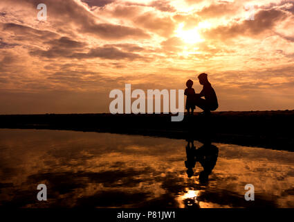 Reflet Silhouette de mère avec son enfant contre le coucher du soleil et reflets en mer. L'activité de la famille asiatique de vie. Banque D'Images