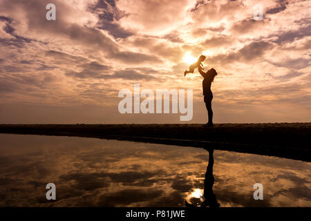 Reflet Silhouette de mère avec son enfant contre le coucher du soleil et reflets en mer. L'activité de la famille asiatique de vie. Banque D'Images